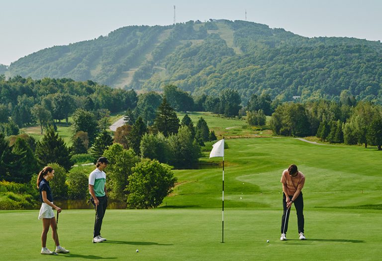 joueurs de golf sur le parcours du Golf Château-Bromont et vue sur Bromont, montagne d'expériences